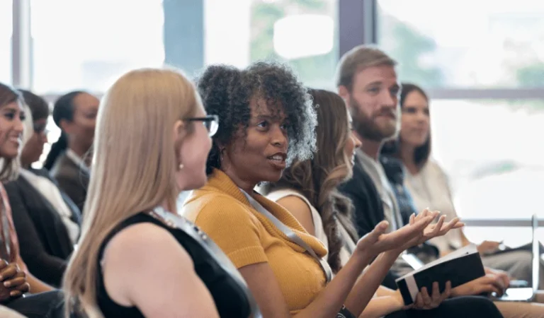 A group of people seated at an event, paying attention and interacting with each other.