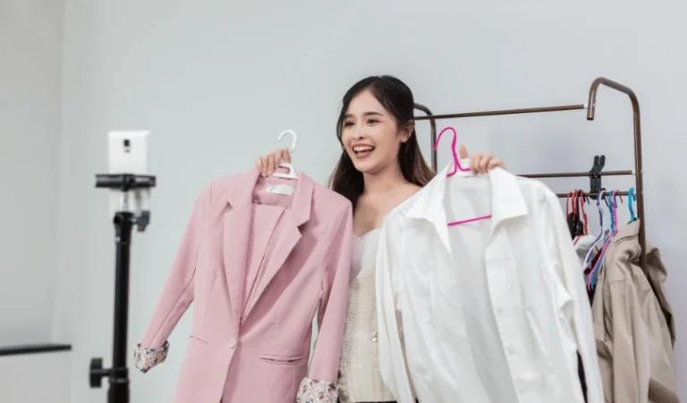 Young woman setting up a fashion shoot with clothing on hangers and a camera tripod.