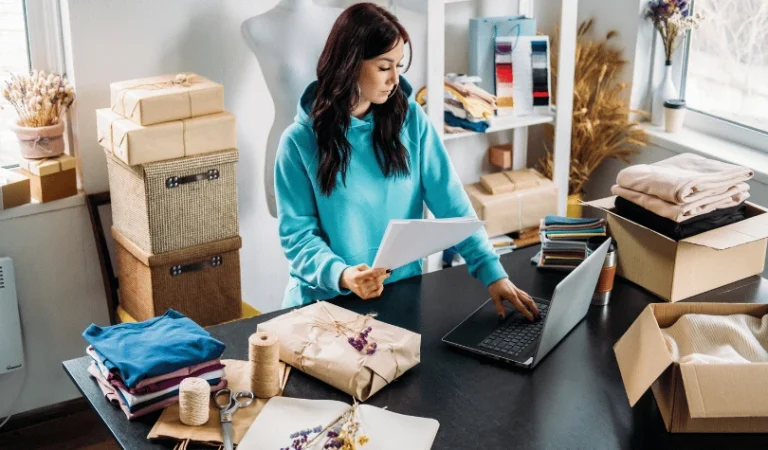 A woman managing online orders and packing items with a laptop and several parcels around.