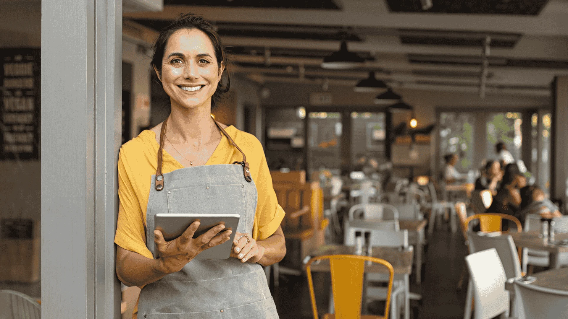 A woman holding a tablet and smiling while standing in a warehouse-like café area.
