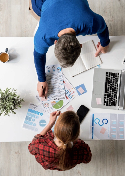 Overhead view of colleagues planning with charts, graphs, and digital tablets around a work table.